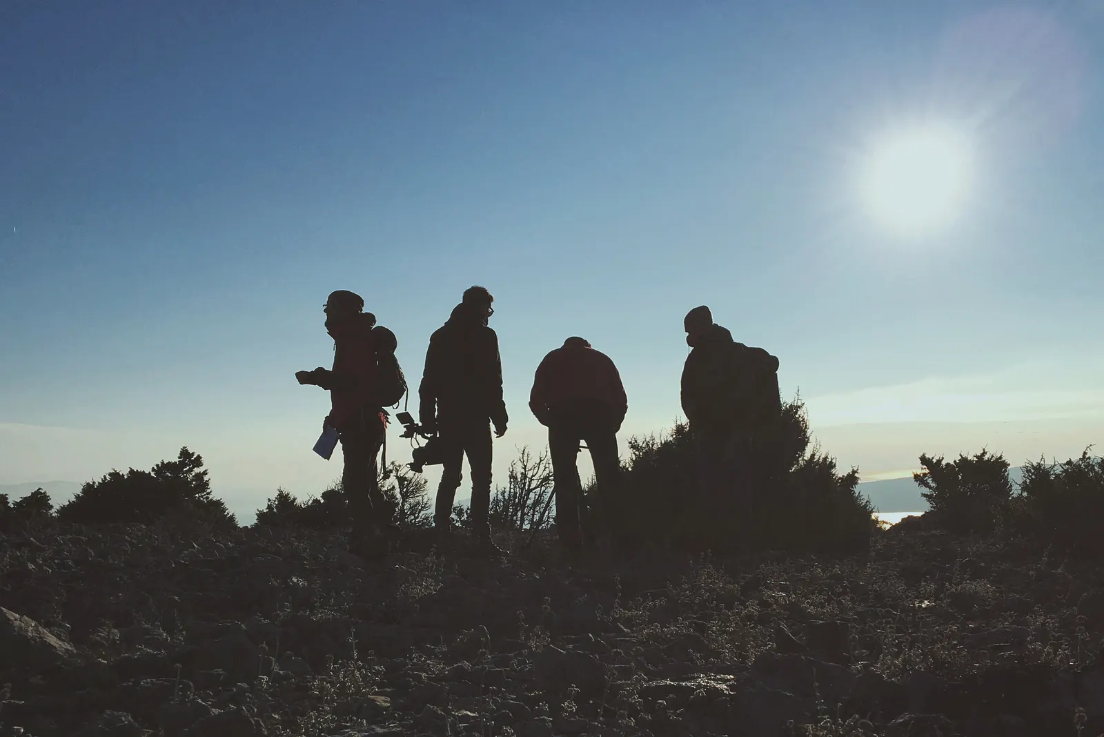 Grupo de excursionistas a contraluz en lo alto de un monte, con el sol brillando en un cielo azul
