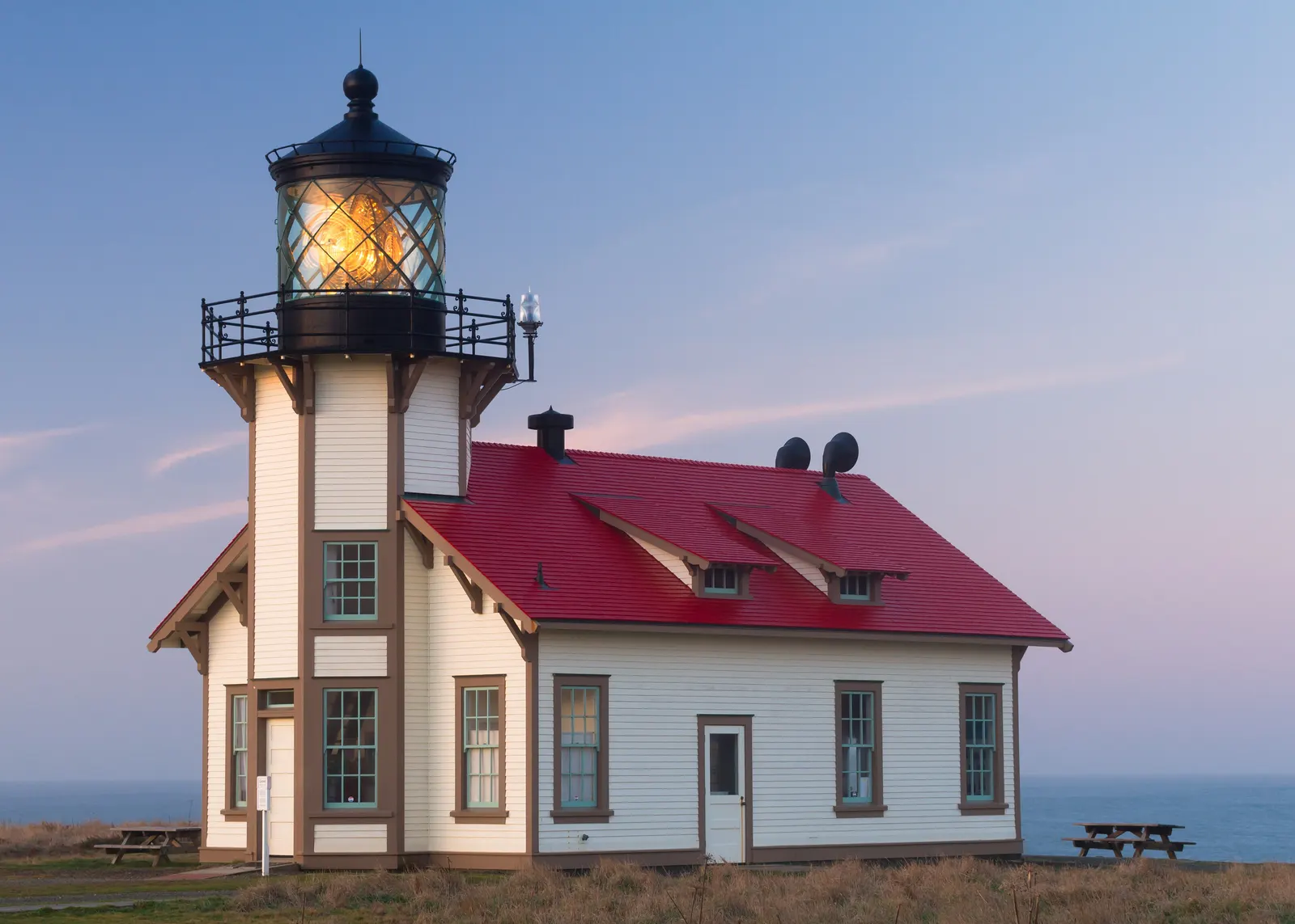 Faro con la linterna encendida al atardecer junto al mar, bajo un cielo sereno